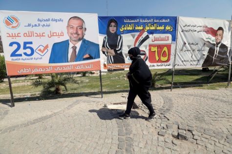 A woman in Baghdad strolls past campaign posters before the parliamentary election on October 10 [Wissam al-Okaili/Reuters]